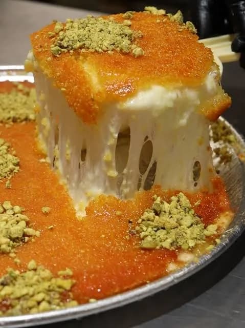 A slice of Palestinian knafeh Nabulsi showing its melted white cheese filling beneath a golden pastry crust.